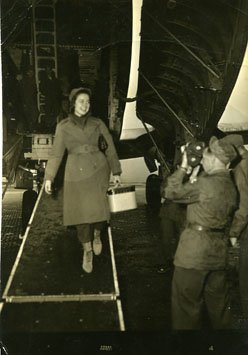 A smiling woman exiting a military plane welcomed by a videographer