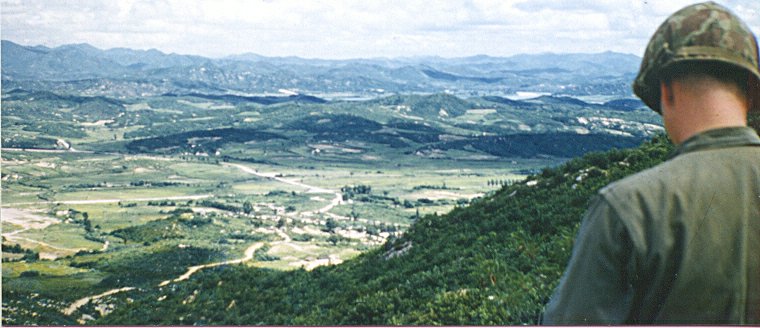 A Korean War soldier standing on the ridge of a battlefield.